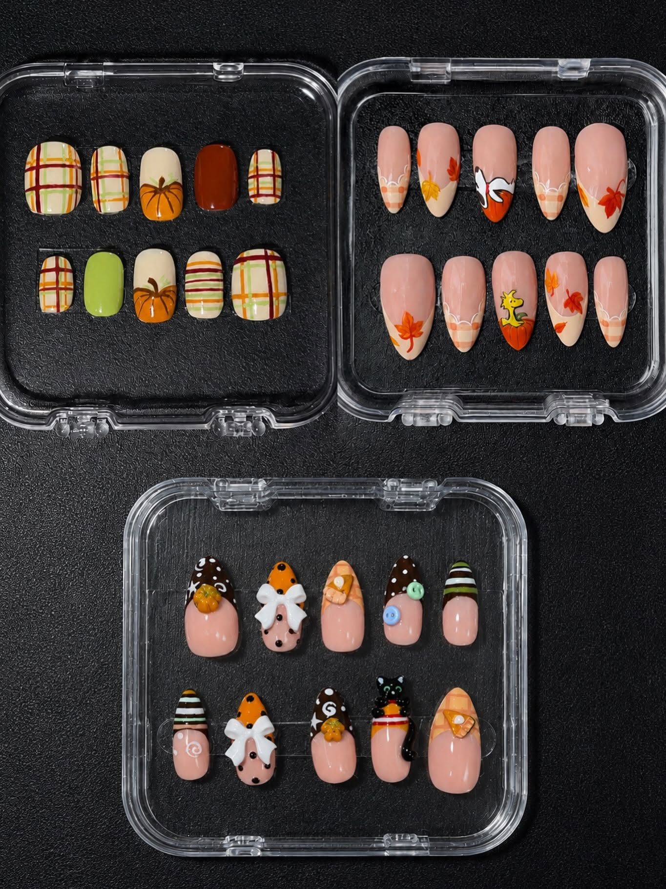 Three boxed press-on sets photographed from above: autumn plaid, falling leaves with a cartoon character, and a Halloween set with bows, a black cat and pumpkins.