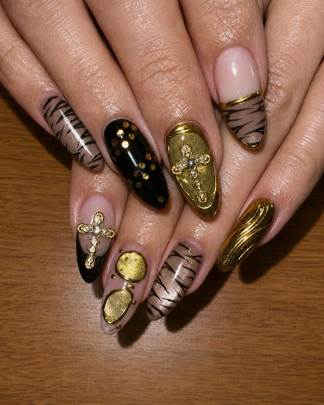 Long almond nails in black and gold chrome with hand-painted tiger stripes, gold studs and gem-set cross charms.
